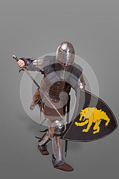 Knight in breaths in a helmet with a sword and shield in battle over grey background