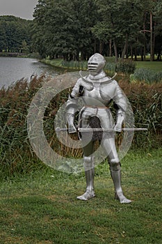 Knight in full armor with a sword against the background of a lake