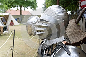 Knight helmet of metal with visor down, replica on a medieval camp with historical armor and weapons, copy space, selected focus