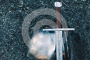 Knight's helmet and shiny metal lying on the ground, it put an old steel sword with leather handle.