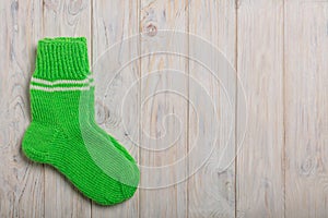 Knit green wool socks on light wooden background.