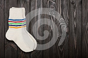Knit white wool socks on dark wooden background.