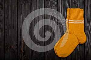 Knit yellow wool socks on dark wooden background.