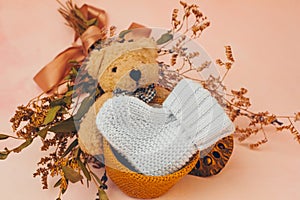 Knitted baby bootee, toy bear and flowers on soft pink background. Congratulations on the birth of a baby concept.