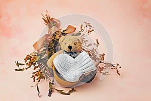 Knitted baby bootee, toy bear and flowers on soft pink background. Expecting a child concept