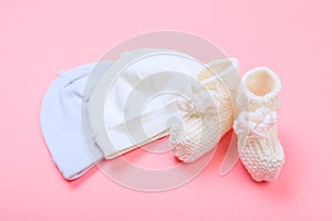 Knitted baby booties and bonnet on pastel pink background
