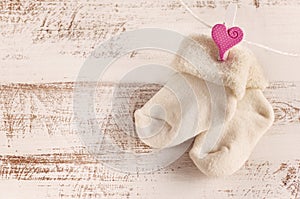 Knitted baby socks with rose heart on the wooden surface