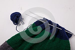 Knitted clothing, accessory in process of making. Knitting needles and ball of threads, yarn on white background. Striped blue,