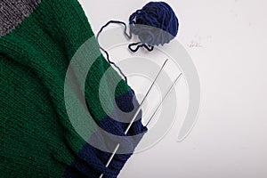 Knitted clothing, accessory in process of making. Knitting needles and ball of threads, yarn on white background. Striped blue,