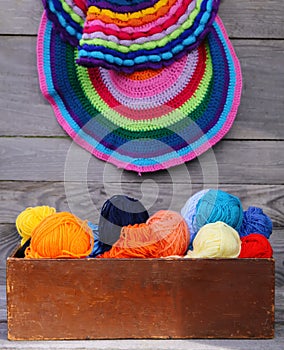 Knitted colorful striped mats and balls of bright woolen yarn in a wooden box on old wood wall background