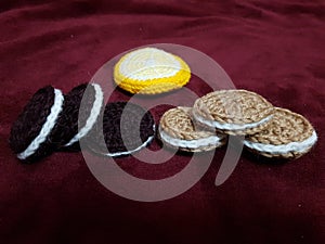 Knitted cookies and a slice of orange lie on a burgundy bedspread.