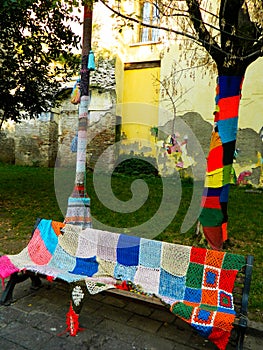 Knitted cover for tree trunk and bench. Knit pattern mosaic on tree. Park in Italy.