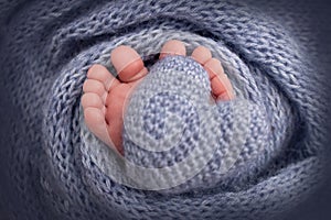 Knitted dark dark blue heart in the legs of a baby. Soft feet of a new born in a dark blue wool blanket. Close-up foot.