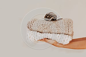 Knitted and folded chunky blanket with knitting needles, yarn ball in human hands on neutral background