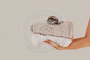 Knitted and folded chunky blanket with knitting needles, yarn ball in human hands on neutral background