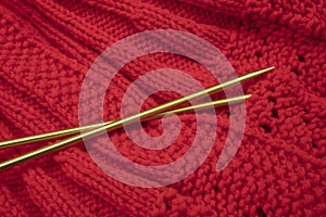Knitted garment in red yarn and golden knitting needles