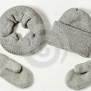 Knitted grey mittens, hat and scarf on white wood background. Fashionable warm clothes