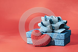 Knitted heart and Blue sparkling gift box with ribbon bow on red background