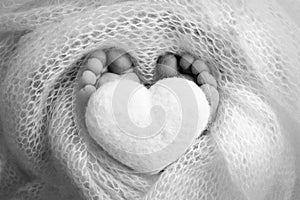 Knitted heart in the legs of a baby. Soft feet of a new born in blanket. Close-up of toes, heels and feet of a newborn.