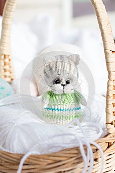 a knitted kitten with knitting needles, colored balls of thread in a basket.