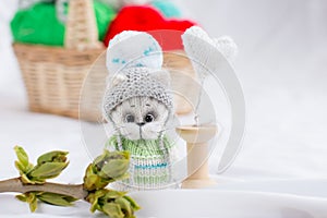 a knitted kitten with knitting needles, colored balls of thread in a basket.