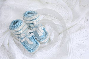 Knitted newborn baby booties on crocheted blanket white background