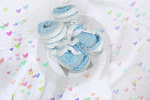 Knitted newborn baby booties on crocheted blanket white background with colorful hearts