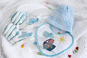 Knitted newborn baby booties, hat and bib on crocheted blanket white background with colorful hearts
