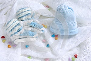 Knitted newborn baby booties and hat on crocheted blanket white background with colorful hearts