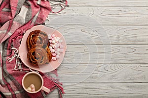Knitted pillows and plaid, buns and coffee on a light wooden background.