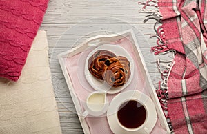 Knitted pillows and plaid, buns and coffee on a light wooden background.