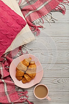 Knitted pillows and plaid, croissants and coffee on a light wood