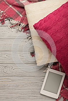 Knitted pillows, plaid and eBook on a light wooden background.