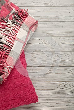 Knitted pillows and plaid on a light wooden background.