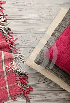 Knitted pillows and plaid on a light wooden background.