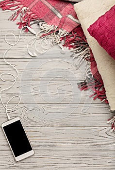 Knitted pillows, plaid and smartphone on a light wooden background.