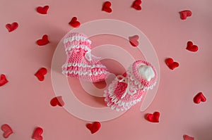 Knitted pink booties baby socks on pink background with hearts