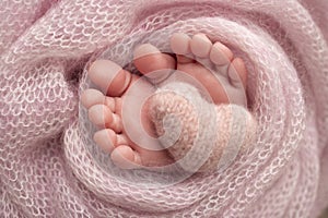 Knitted pink heart in the legs of a baby. Soft feet of a new born in a pink.