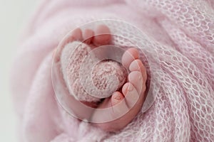 Knitted pink heart in the legs of a baby. Soft feet of a new born in a pink