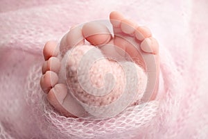 Knitted pink heart in the legs of a baby. Soft feet of a new born in a pink wool blanket.