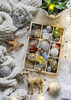 Knitted plaid, box of christmas toys, light garland on fluffy carpet, top view. Christmas background