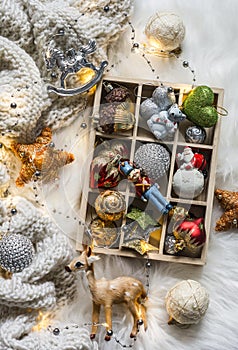 Knitted plaid, box of christmas toys, light garland on fluffy carpet, top view. Christmas background