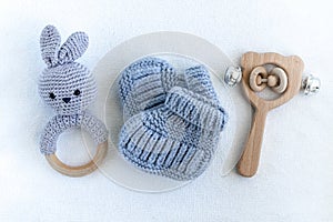 Knitted shoes for newborns, handmade knitted amigurumi rabbit and wooden baby toy on white background.