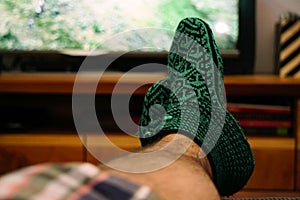 Knitted snoozies on man`s foot watching tv chilling at home