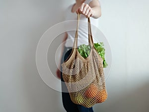 Knitted string bag with products oranges and greens. the shopper is beige. crochet eco bag in the hand of a girl in a