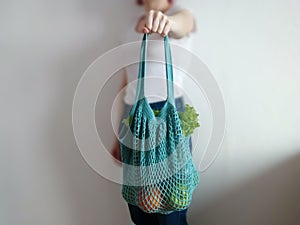 Knitted string bag with products oranges and greens. the shopper is blue. crochet eco bag in the hand of a girl in a