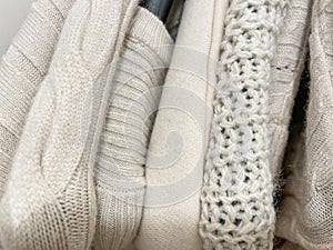 Knitted sweaters and jumpers of beige cream color on hangerts in stack photo from above.