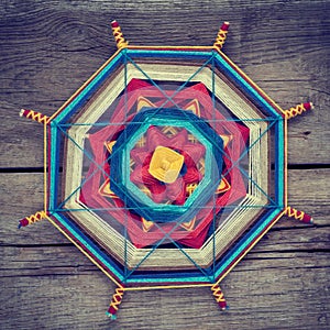 Knitted tibetan mandala from threads on wooden background