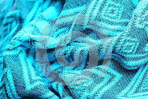 Knitted turquoise-coloured fabric with soft folds and with a geometric drawing view from the top in light from the window.