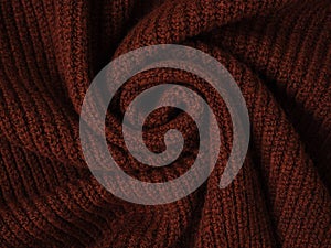 Knitted warm brown sweater or scarf. Cozy composition in the home atmosphere. Chocolate wool fabric texture close up